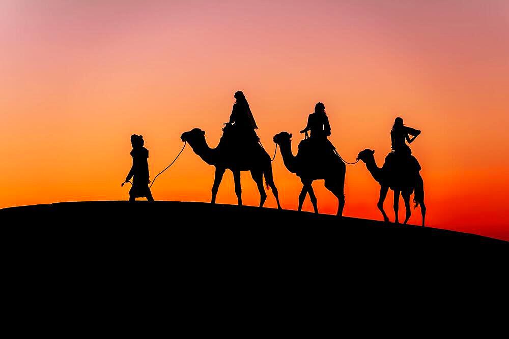 Three passengers and their handler travel in the Saharan Desert in Morocco