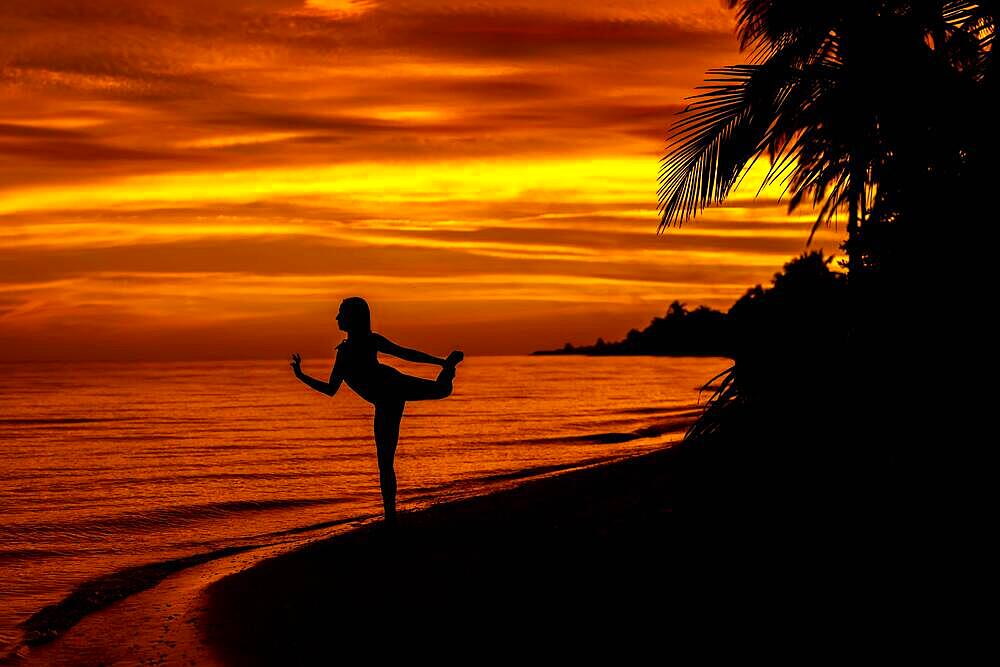 The sun rises over the Gulf of Mexico near Sinanche Yucatan Mexico with a nude latin model posing against the colorful sky