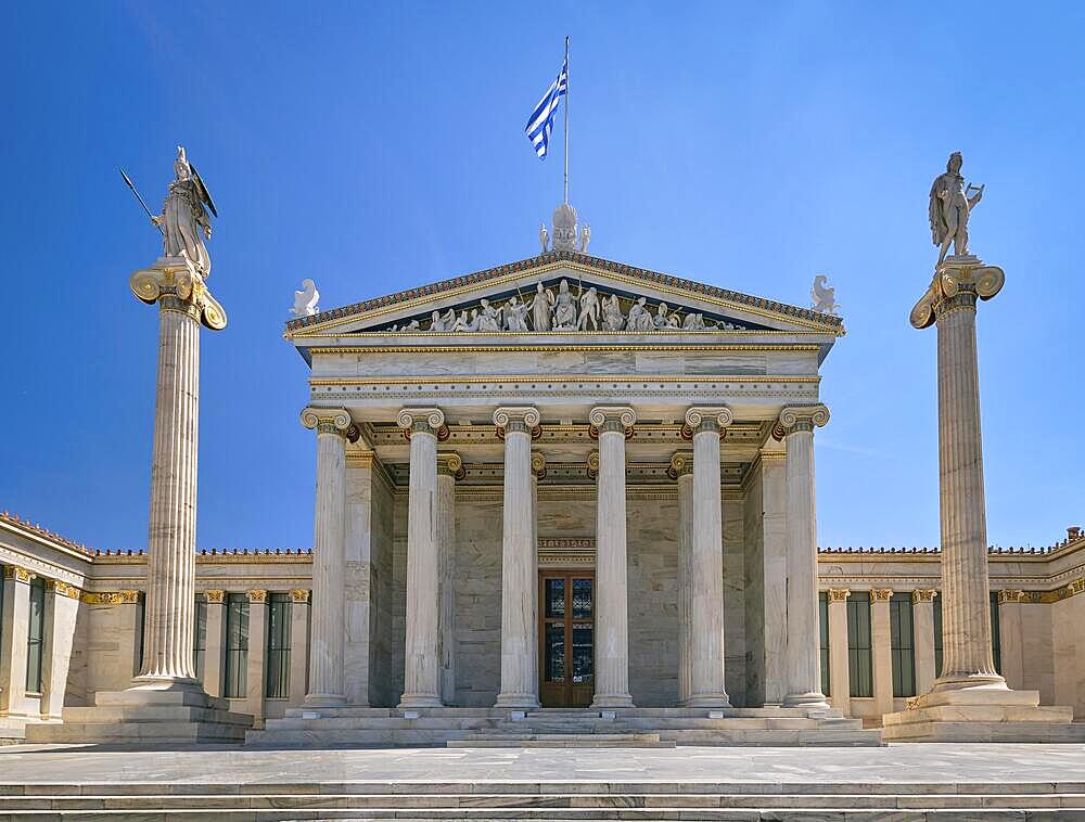 Marble main entrance of Academy of Athens, national research center, columns or pillars with Athena, ancient Greek goddess and patron of city, and Apollo, ancient Greek god and patron of arts and science. National Greek flag. Summer day, blue sky