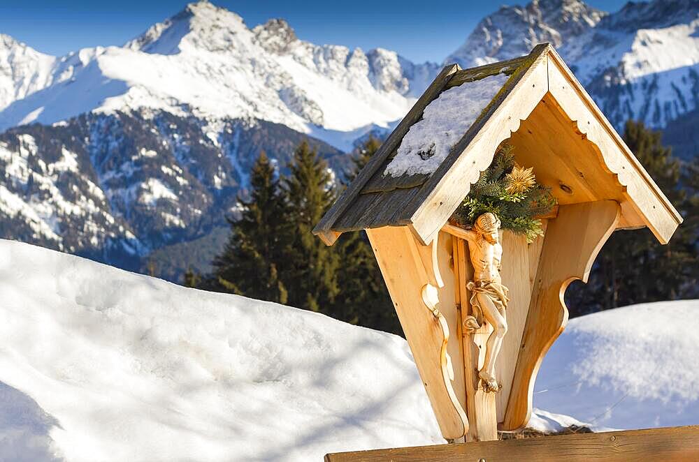 A wooden sculpture of crucified Jesus Christ on the background of the Alps mountains in winter. View of the mountains. Religion and culture. Austria