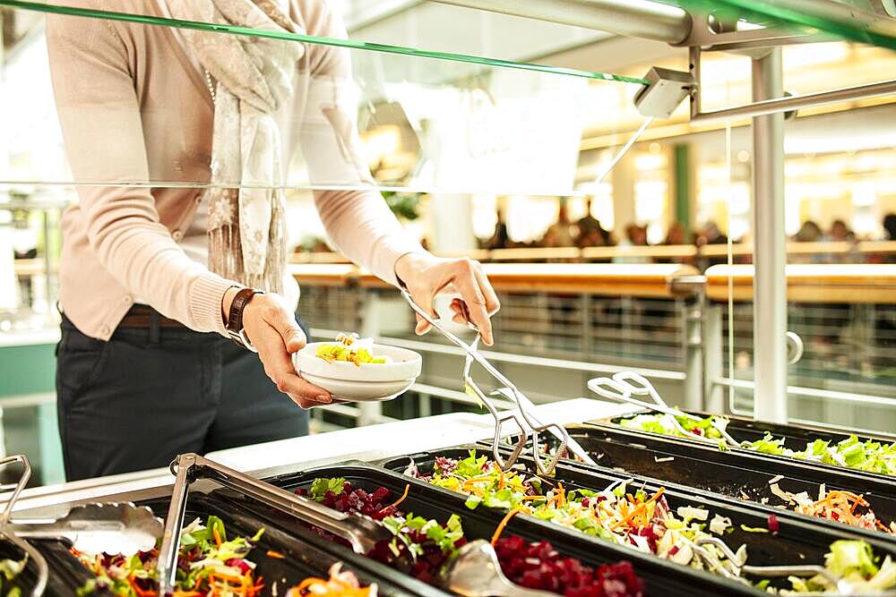 Fresh salads in a salad bar, a woman serves herself at the buffet