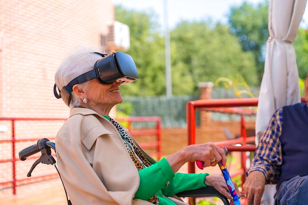 An elderly woman with the nurse looking through virtual reality glasses in the garden of a nursing home, vr glasses