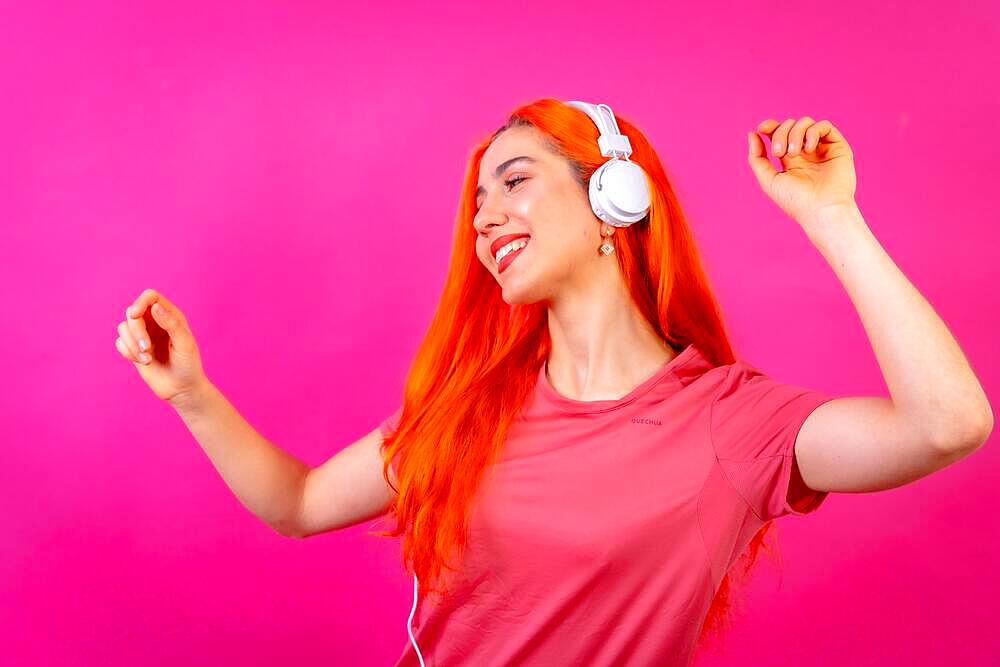 Redhead woman in studio photography dancing smiling on a pink background