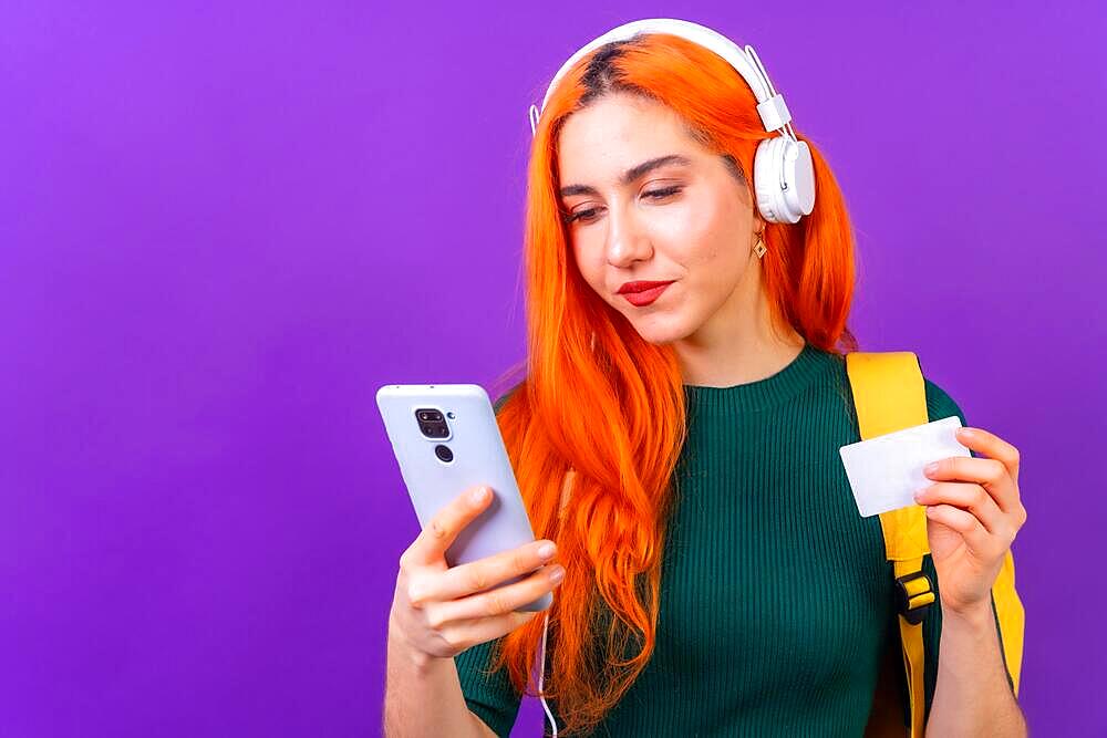 Redhead woman in studio photography online payment with mobile on a purple background