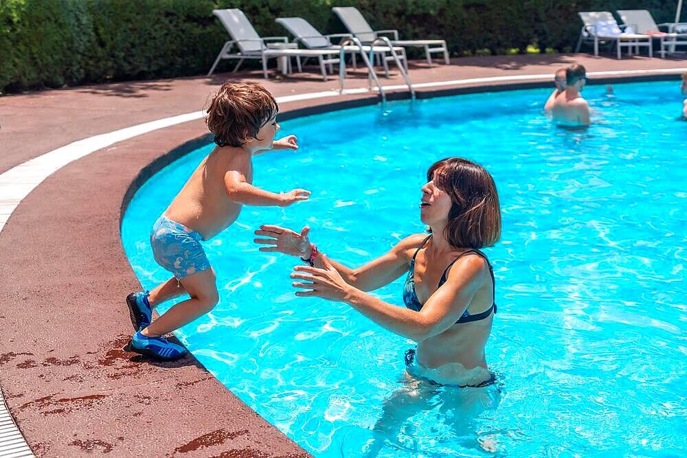 Mother and son in the pool on summer vacation, jumping into the water on top of the mother