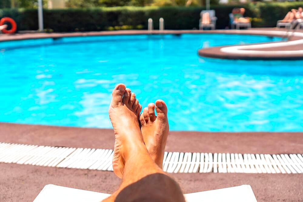 Men's legs lying on a deck chair overlooking the water, sunbathing by the pool of the hotel resort