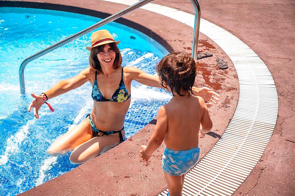 Mother and son in the pool on summer vacation, moment of love giving his mother a kiss