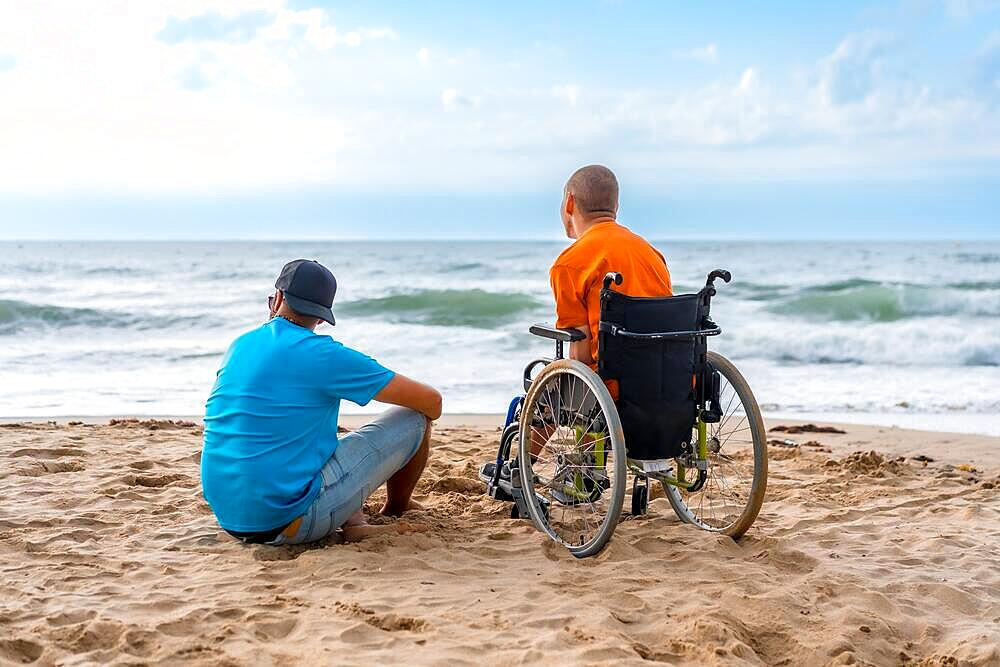 Portrait a disabled person in a wheelchair on the beach with a friends sitting looking at the sea