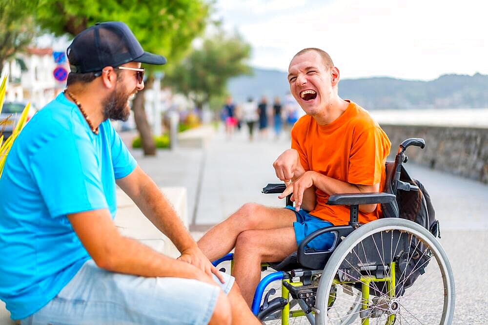 A disabled person in a wheelchair with a friend on summer vacation having fun laughing a lot by the sea