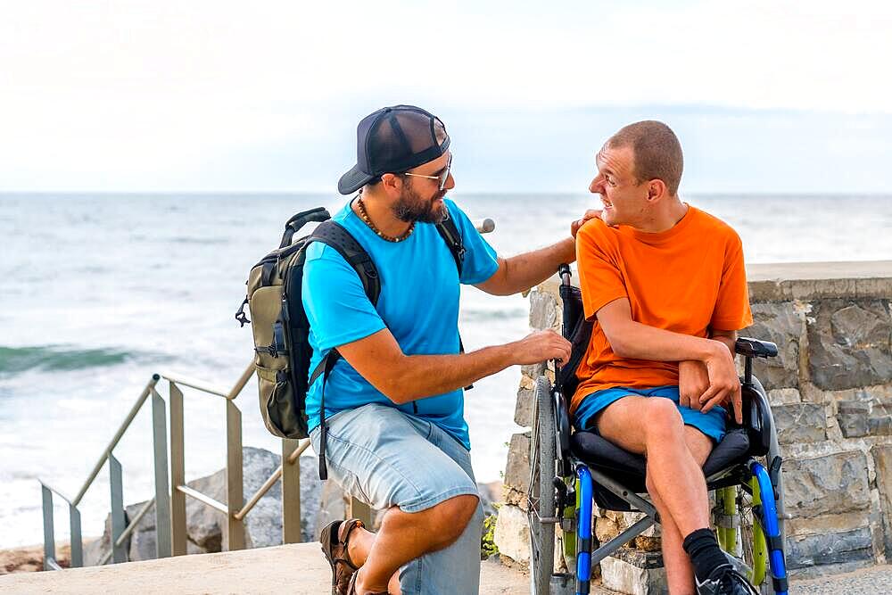 A disabled person in a wheelchair with a friends on summer vacation talking by the sea