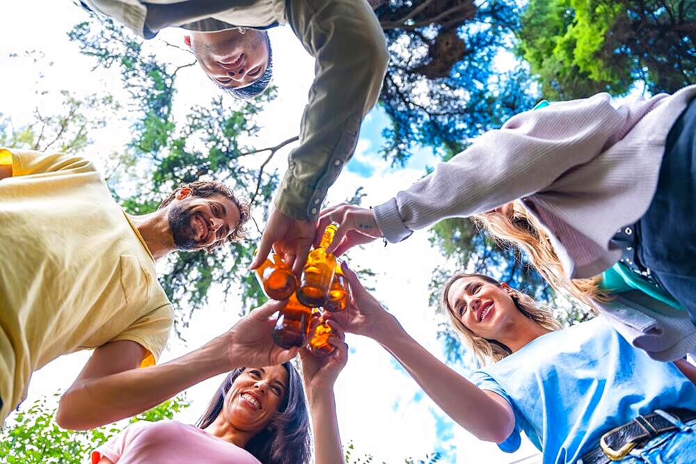 Nadir shot of a group of multi ethnic friends sitting in the city park toasting with bottles of beers