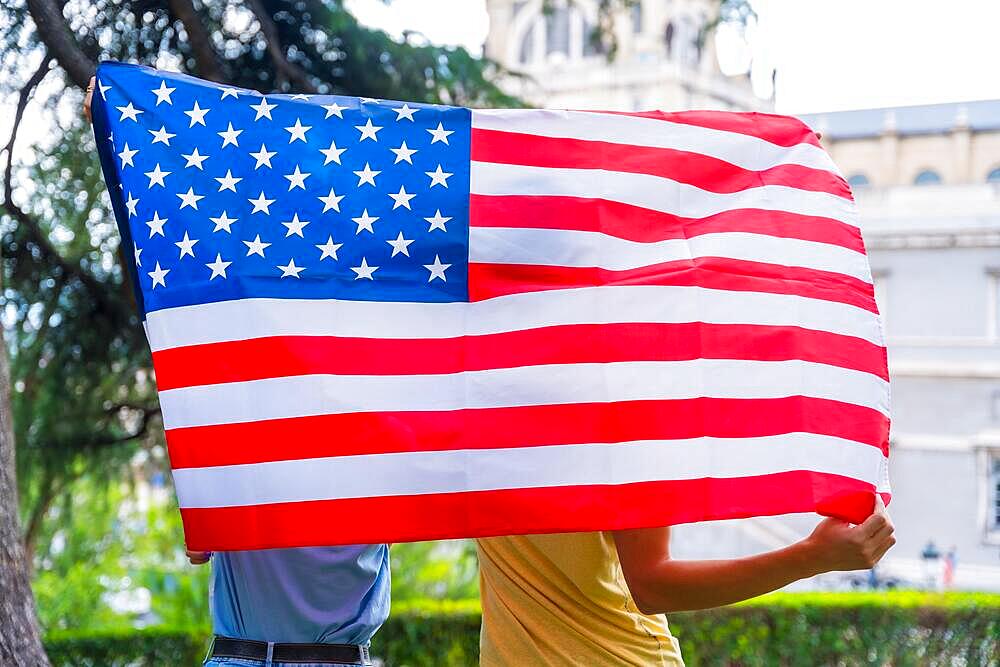 Couple in the city with usa flag, boy and girl on their backs. Patriots proud of their nation, independence day