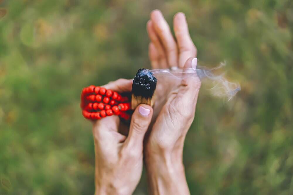 Top angle view of a palo santo or a holy sacred tree stick, burning with aroma smoke held by woman's hands over nature background