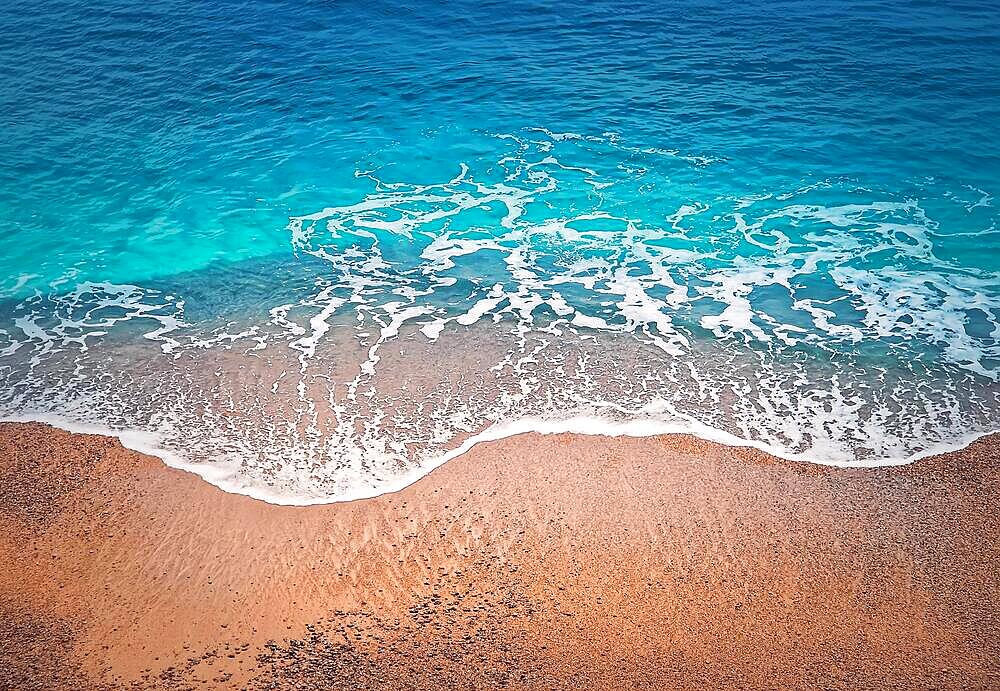 Blue ocean waves hits the shoreline. Beautiful texture of turquoise sea water and golden sandy beach. Tropical summer seaside background