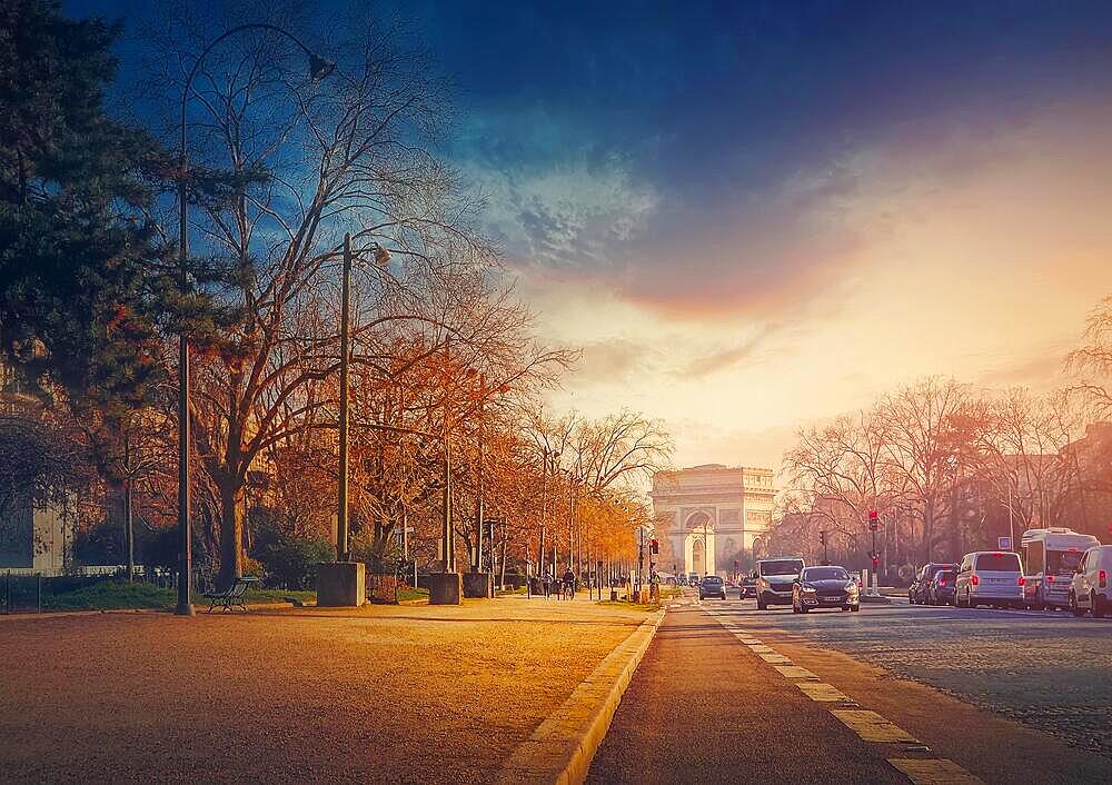 Triumphal Arch (Arc de triomphe) in Paris, France. The famous historic landmark in sunset light seen from the city street with busy traffic