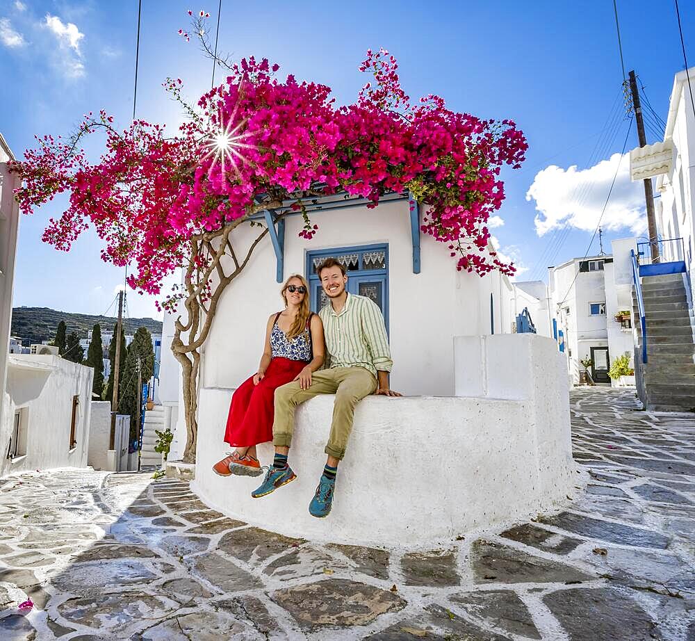 Young couple in love, white Cycladic house with blue door and pink bougainvillea, with sun star, picturesque alleys of Lefkes village, Paros, Cyclades, Greece, Europe