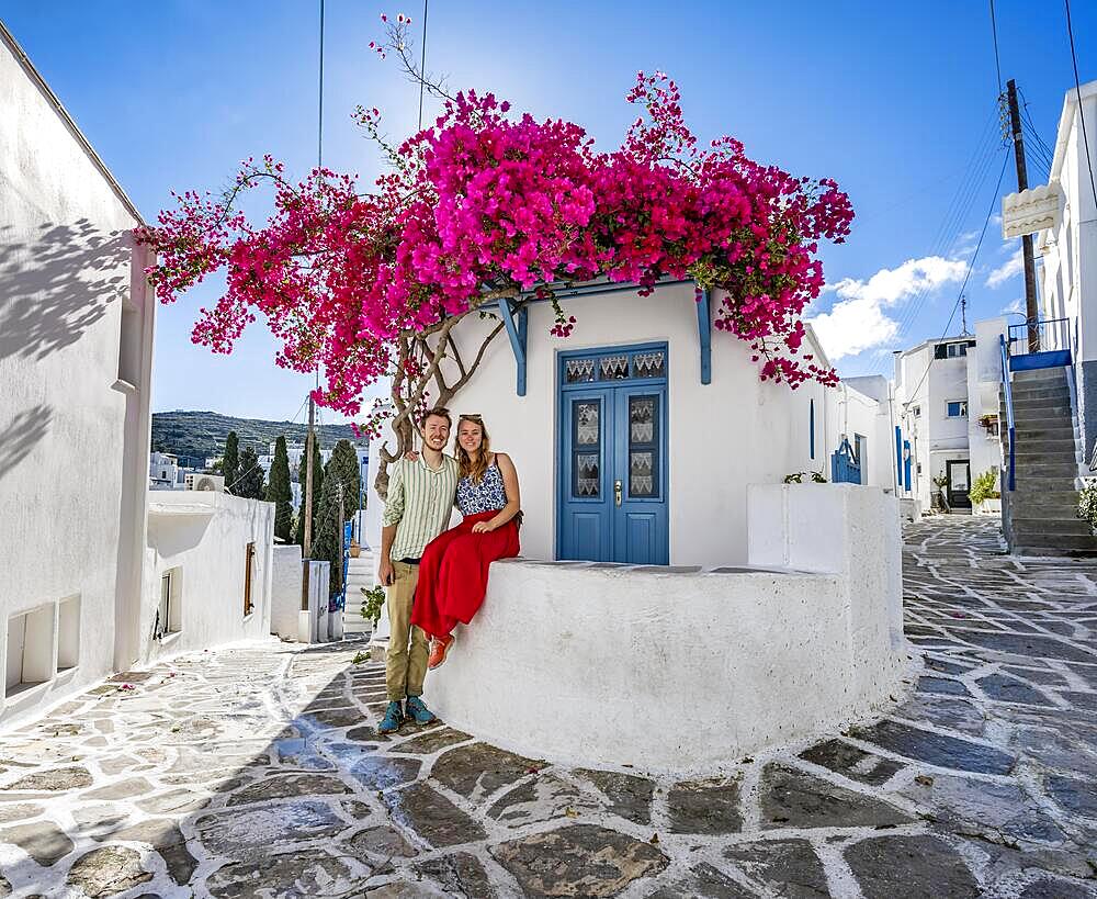 Young couple in love, white Cycladic house with blue door and pink bougainvillea, with sun star, picturesque alleys of Lefkes village, Paros, Cyclades, Greece, Europe