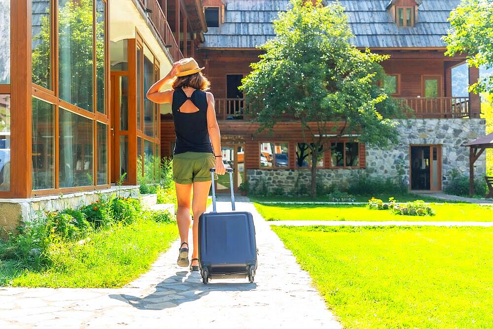 Tourist woman with a suitcase on rural vacation arriving at a mountain cabin