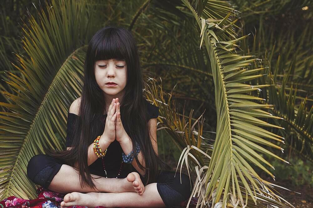 Sweet girl meditating near palm