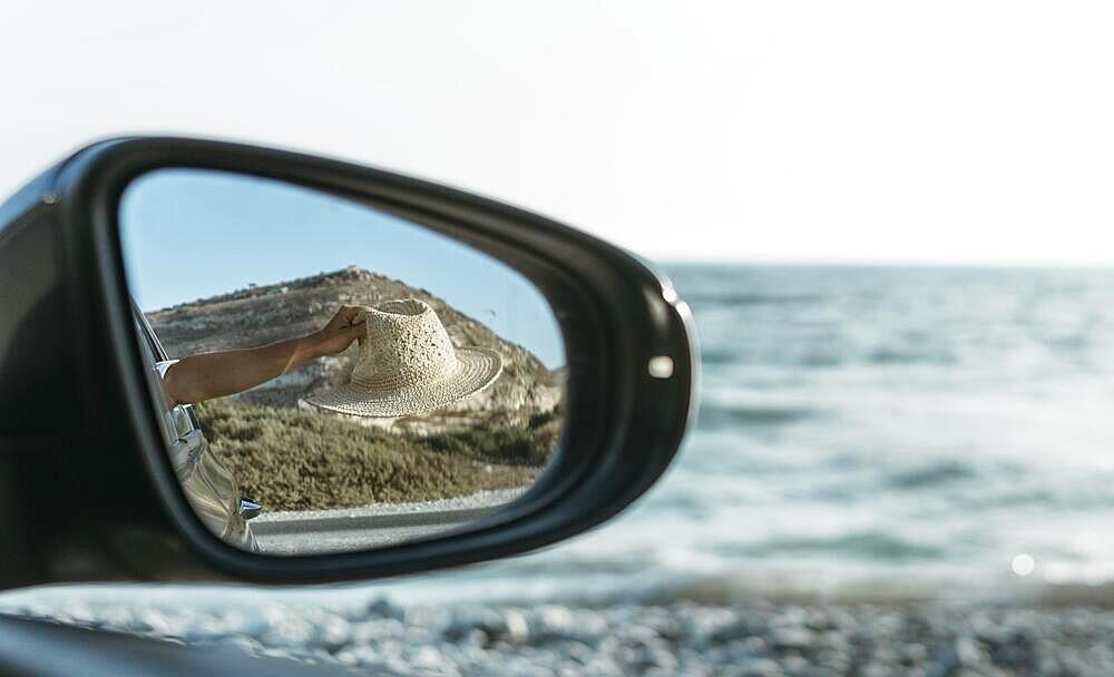 Woman holding hat out window car mirror view