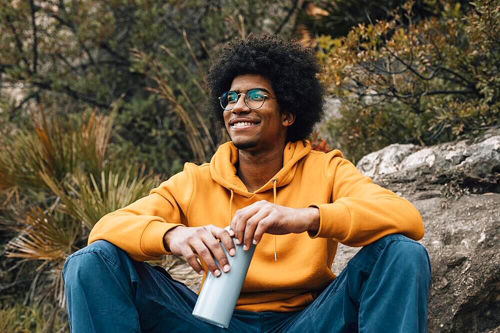 Portrait smiling young african man holding water bottle hand looking away