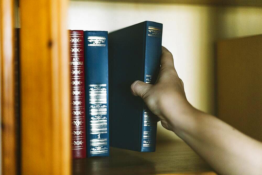 Crop hand picking book from shelf