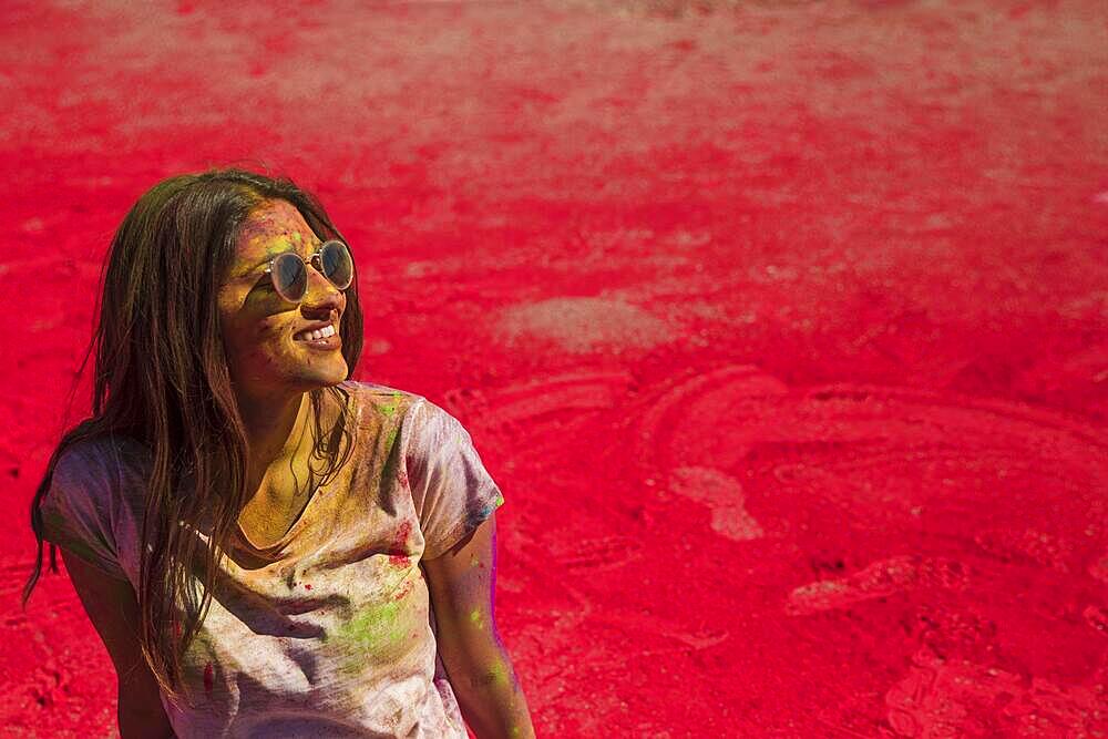 Portrait smiling young woman wearing sunglasses messing holi color