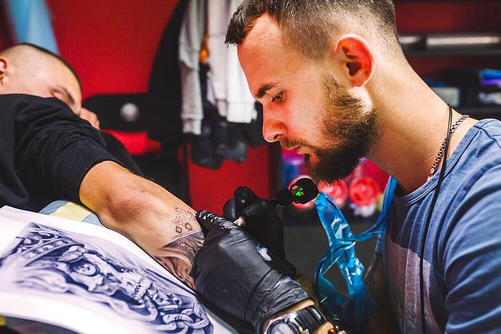 Adult man working with tattoo pen arm