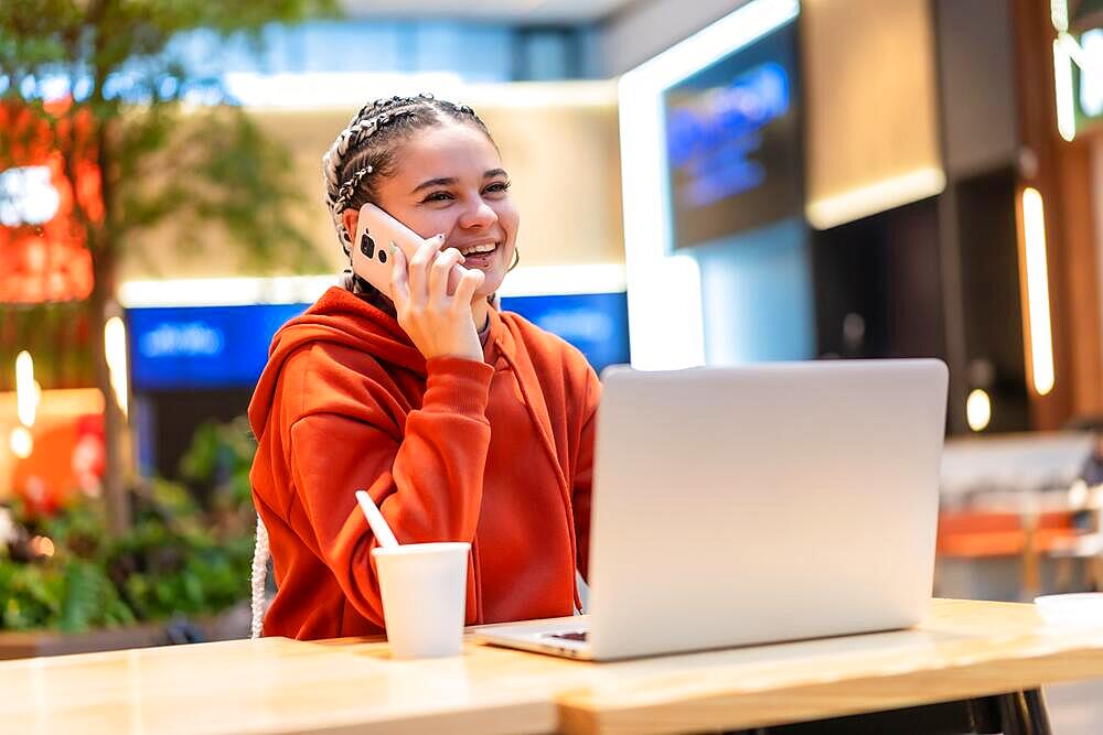 Alternative girl with white braids using a computer in a shopping mall, smiling making a call