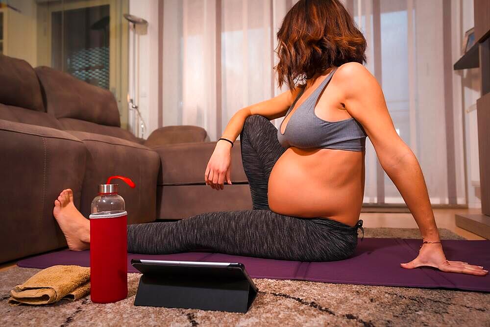 Detail of a young pregnant caucasian woman with gray t-shirt performing pilates exercise. Online exercises in prepartum classes, wellness during pregnancy