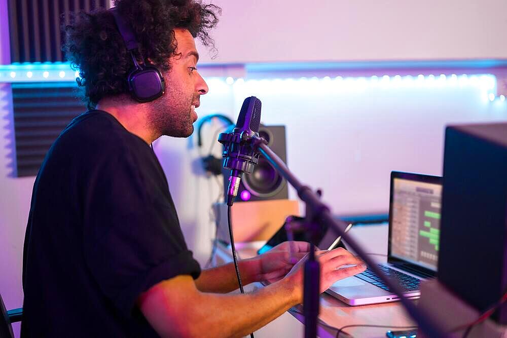 Side view of a musician recording a podcast using microphone and laptop