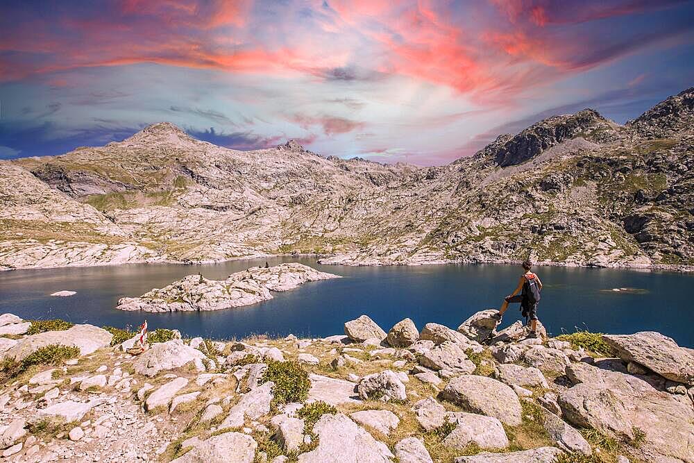 A young woman on top of a stone looking at the Ibon de Estanes in the Pyrenees at sunset. Spain