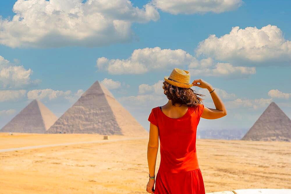 A young tourist in a red dress looking at the Pyramids of Giza, the oldest Funerary monument in the world. In the city of Cairo, Egypt, Africa