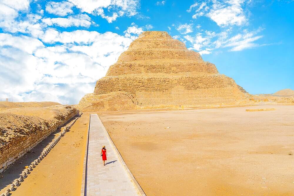 A young girl in a red dress walking in the Stepped Pyramid of Djoser, Saqqara. Egypt. The most important necropolis in Memphis. The first pyramid in the world