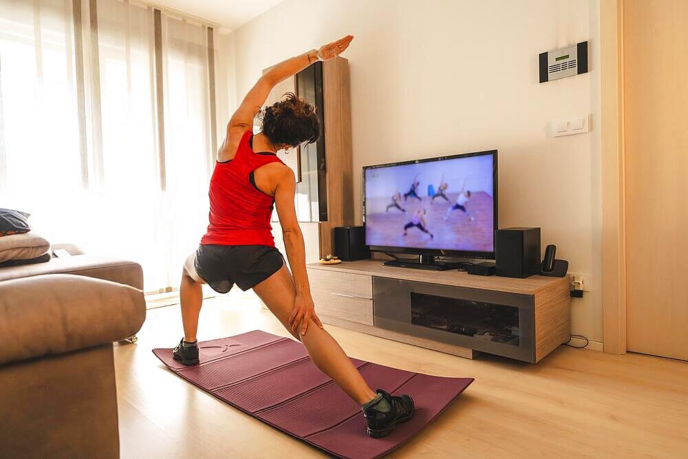 A young woman doing stretching in the room following the instructions of the online teacher. Sport in the covid19 quarantine at home