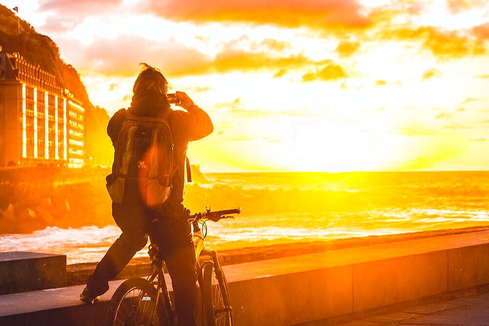 A tourist taking a photo with his cell phone at sunset in the city of San Sebastian, Gipuzkoa. Basque Country