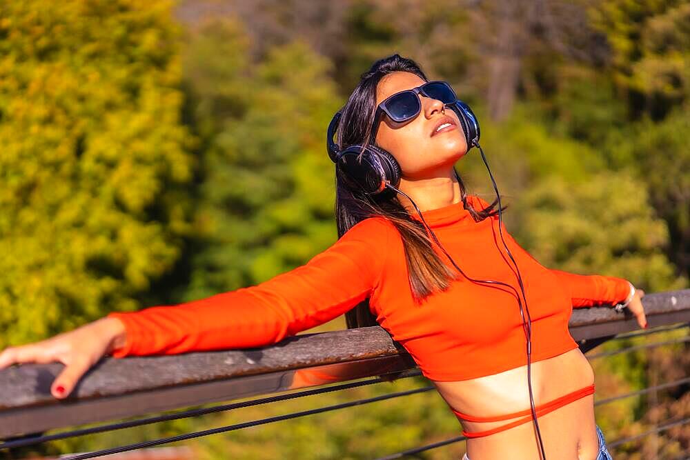 Lifestyle, brunette Caucasian girl enjoying music with headphones in a park. Young girl in red t-shirt and jeans, copy space and paste