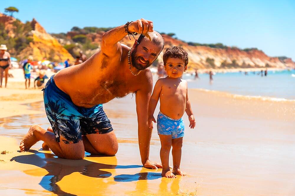 Father playing in the sand with son, Praia do Barranco das Belharucas beach, Albufeira, Algarve. Portugal