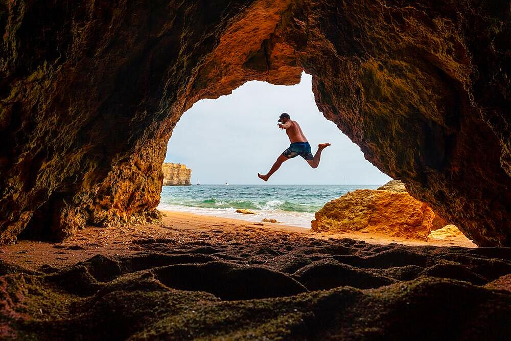 A man jumping into the natural cave in the Algarve on the beach at Praia da Coelha, Albufeira. Portugal