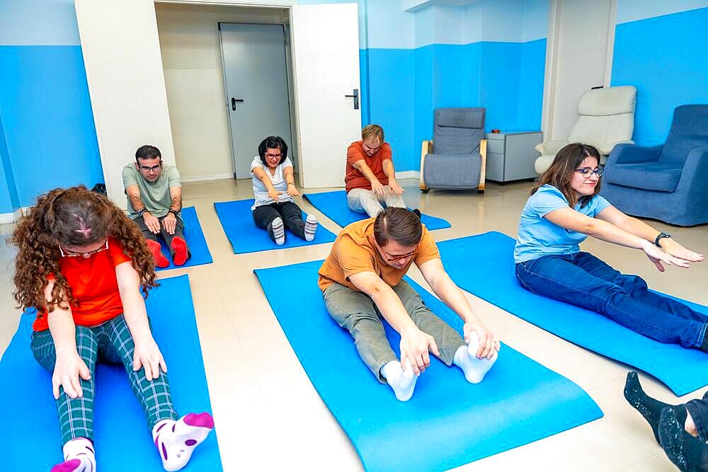 Group of adult intellectual disabled people stretching sitting on a mat during yoga class