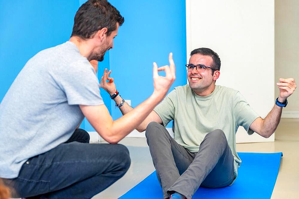 Yoga instructor helping a hand to a disabled man during a yoga pose sitting on the mat in the class