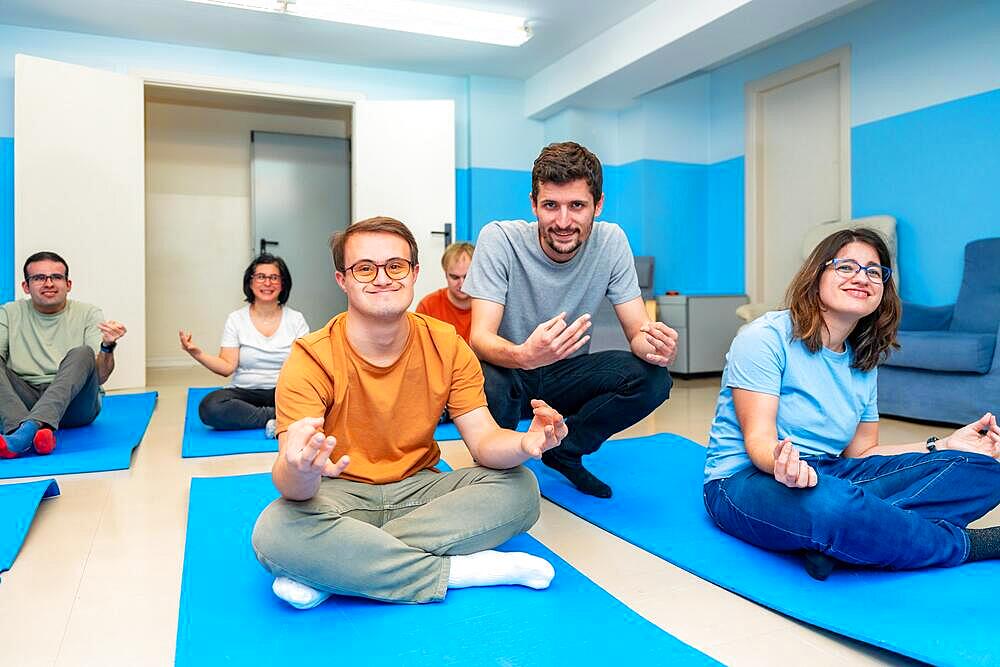 Friendly male yoga instructor directing a class with people with special needs and down syndrome