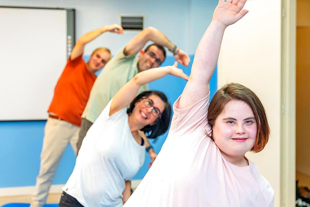 Focus on a woman with down syndrome and a group of people with special needs stretching in the gym