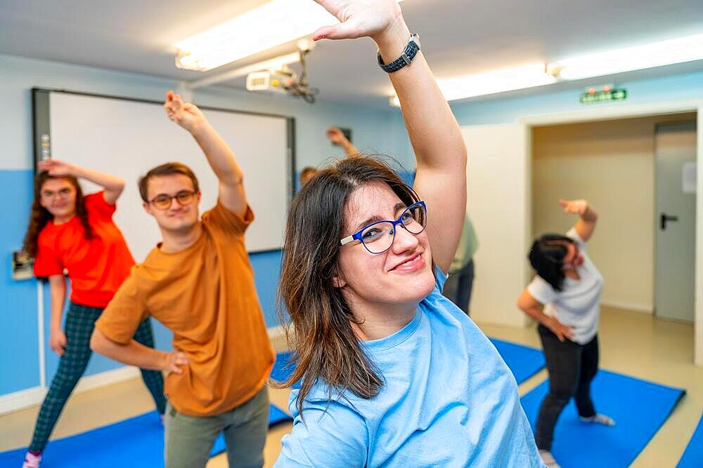 Happy people with special needs exercising in a gym smiling and looking at camera standing stretching the back