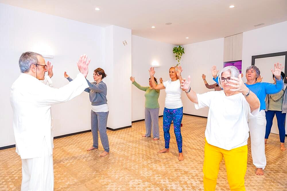 Qi gong male mature teacher leading a class full of mature women in a indoor centre