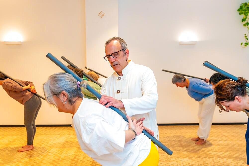 Qi gong class members using tube to stretch the back with the guidance of a male instructor