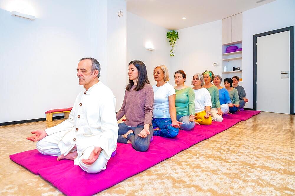 Yoga instructor and women meditating on a mat sitting in line in lotus position