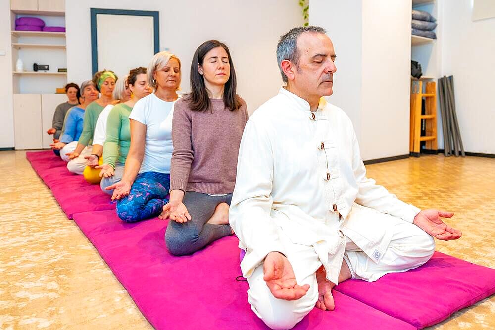 Yoga teacher leading a meditation in a community sitting on mat with lotus position