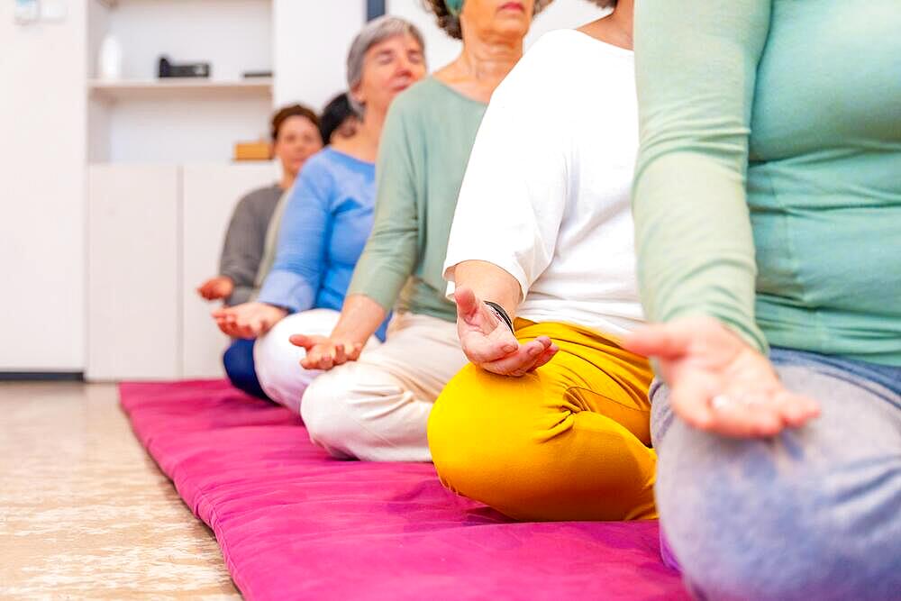 Cropped photo with copy space on left of part of people meditating on a mat in lotus position