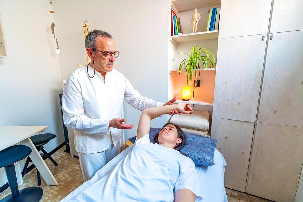 Qi gong masseur performing massage and stretching to a patient lying on stretcher in a clinic